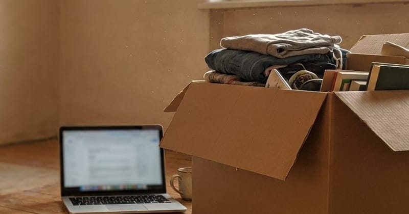 A half-packed cardboard box beside an open laptop on a wooden floor